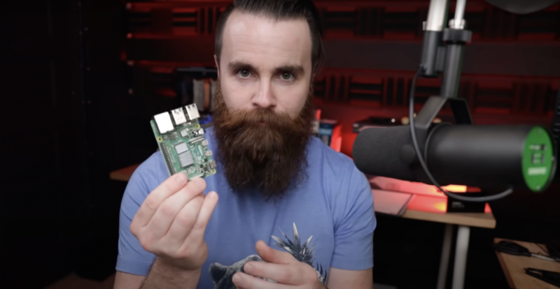 Network Chuck holding a Raspberry Pi 4 next to his broadcasting microphone