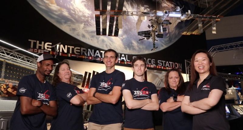 Team ISS posing in NASA t shirts in front of the ISS mimic