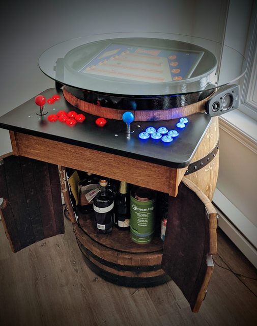 A beer barrel with drinks inside two opening doors cut into the front of the barrel and a retro arcade console serving as the lid of the barrel with joystick and buttons on a ledge in front 