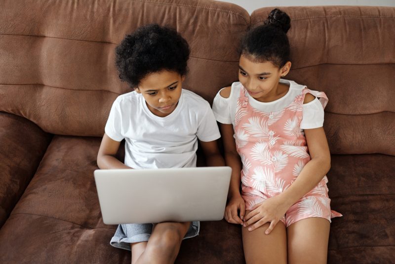 Two siblings sit on a sofa looking at a laptop