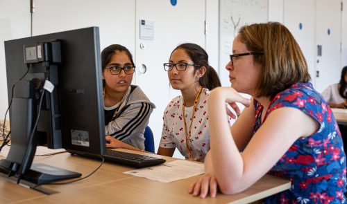 Woman computing teacher and female students at a computer.