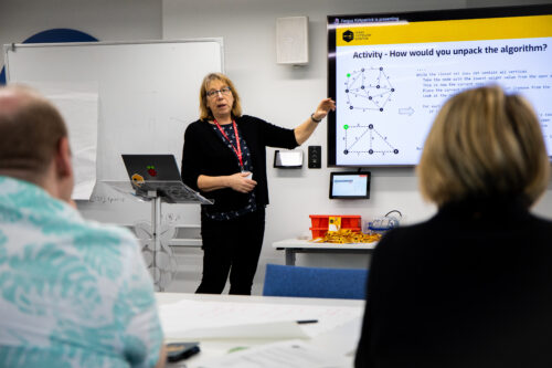 A woman teacher presents to an audience in a classroom.