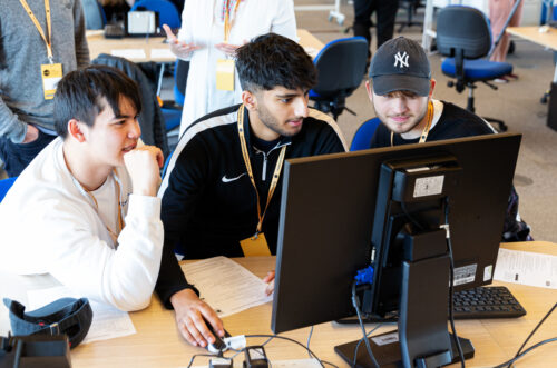 Three teenage boys do coding at a shared computer during a computer science lesson.