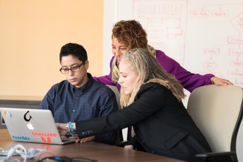 Three women discuss something while looking at a laptop screen.