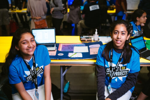Two teenage girls participating in Coolest Projects show off their tech project.