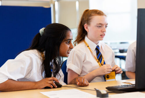 Two female learners code at a computer together.